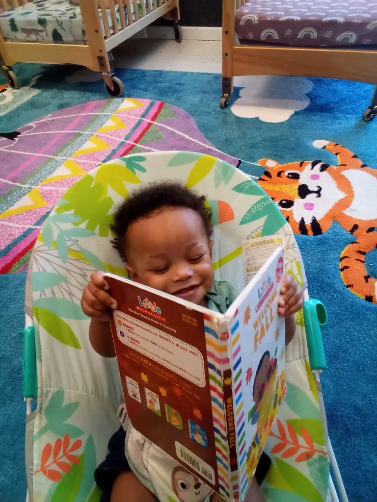 A smiling baby holds open a board book.