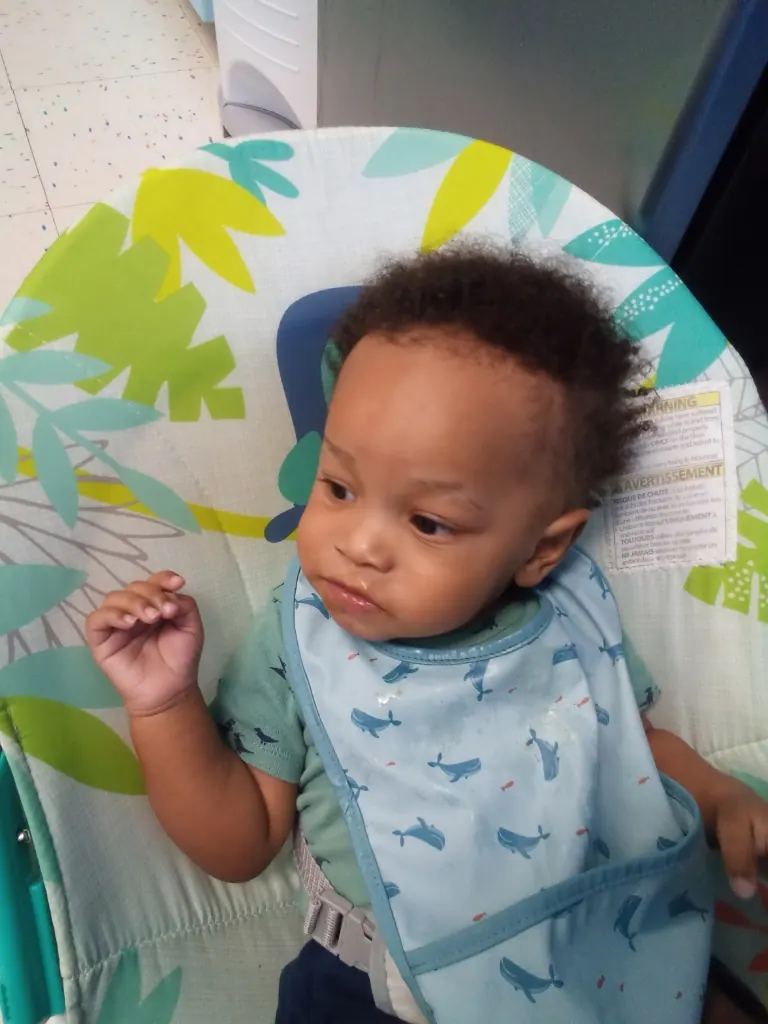 A baby in a bib, sitting in a bouncer at lunch.