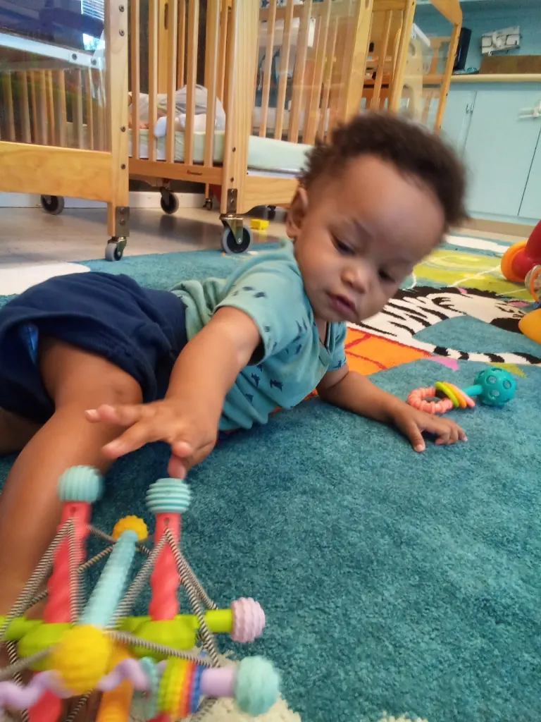 A baby reaches for a toy while pushing up on one arm.