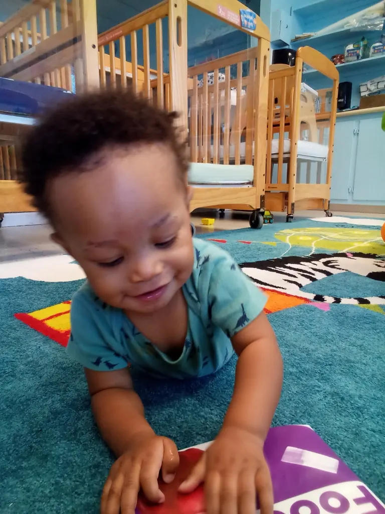 A baby smiles during tummy time on a play mat.