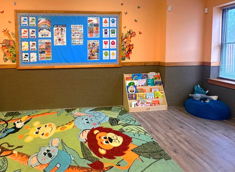 A cozy Falmouth classroom with a jungle-animal rug, a picture-book display, and colorful learning charts on the wall.
