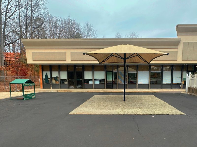 The covered outdoor patio and play area behind the Falmouth center, with a large shade umbrella and a farmers-market play stand.