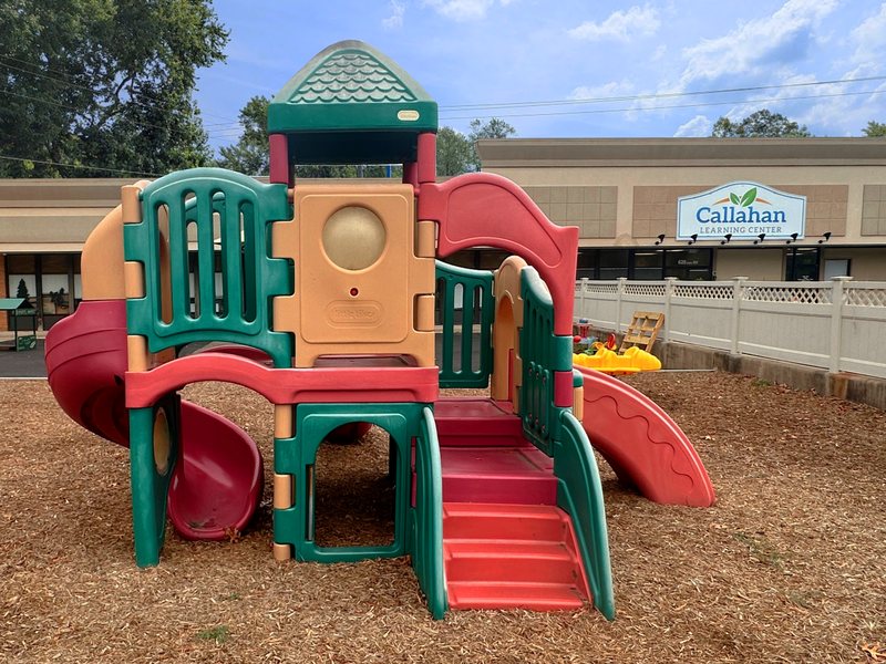 The Falmouth playground with a multi-level climbing structure and slides on a soft mulch surface, the center building behind.