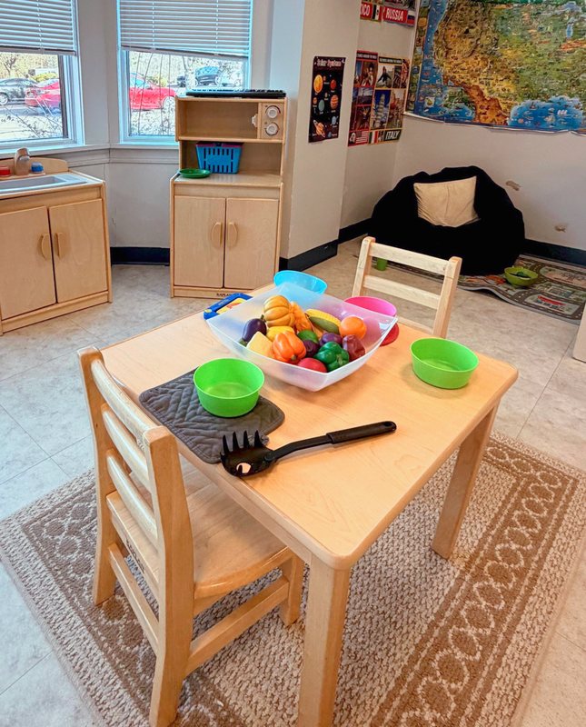 A Locust Grove dramatic-play classroom with a play kitchen, a table set with play food, a world map, and a cozy reading corner.