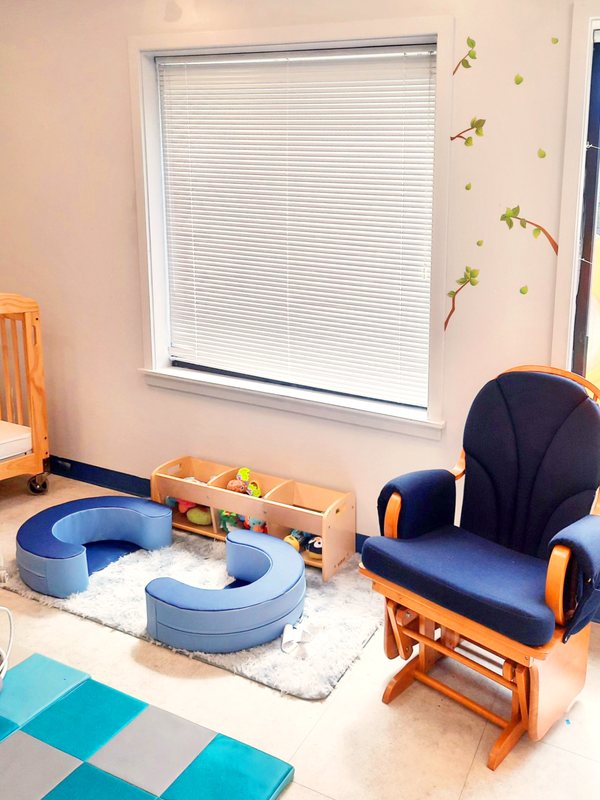 A calm Locust Grove infant room with a navy glider rocker, a soft crescent play set, a wooden toy shelf, and a crib.