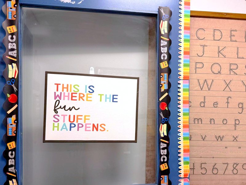 A Locust Grove classroom door with a sign reading This is where the fun stuff happens, beside a handwriting alphabet chart.