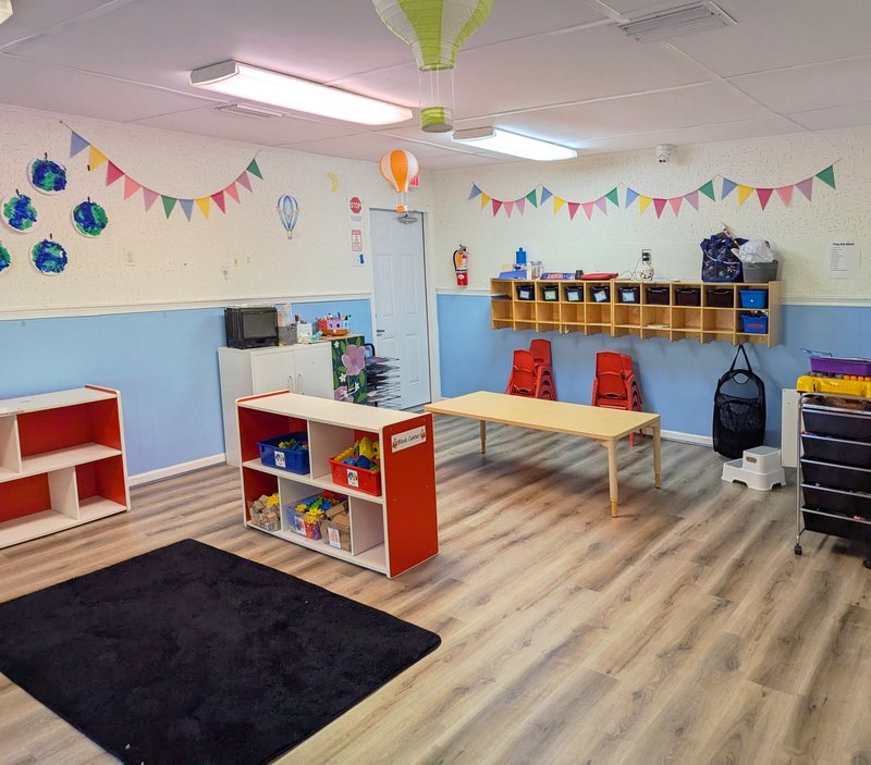 A bright Maple Grove classroom with children's earth-themed artwork, pennant bunting, coat hooks, and low storage shelves.