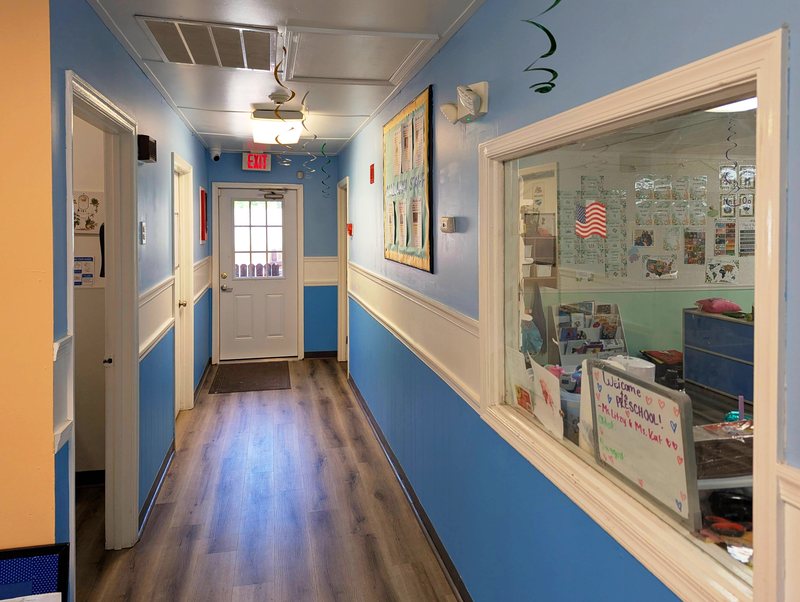 A Maple Grove hallway in cheerful blue, with a window looking into a preschool classroom full of children's artwork.