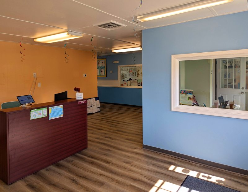 The Maple Grove reception desk and sign-in area, with a warm orange accent wall and a window into the office.