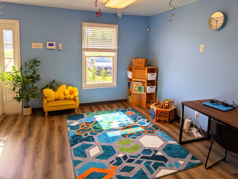 A bright Maple Grove family room with a sunny yellow flower-shaped loveseat, a geometric rug, and a picture-book shelf.
