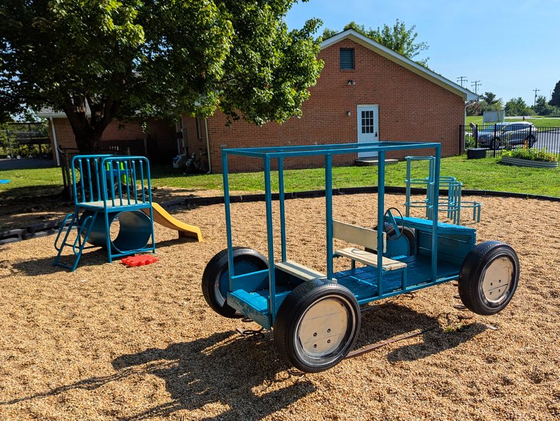 A blue car-shaped play structure and a climber with a slide on the Maple Grove playground, the brick building behind.